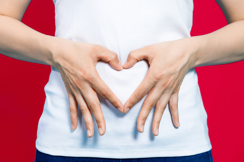 person holding heart shape with their hands over their stomach